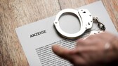 Person zeigt auf einen Zettel mit einer polizeilichen Anzeige und einer Handschelle.