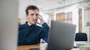Mann schaut verwirrt auf seinen Laptop.