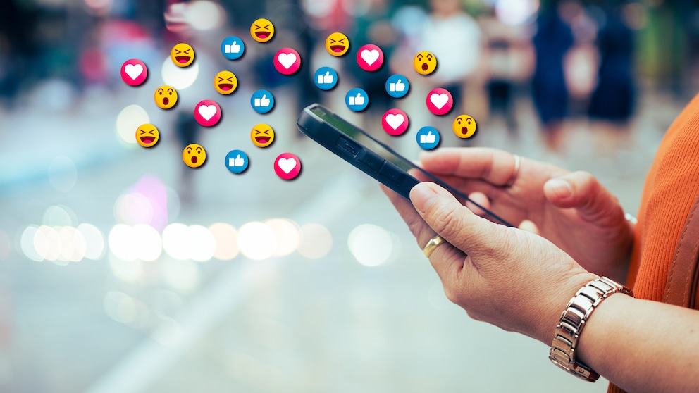 Emojis schweben über dem Smartphone, das eine Person nutzt.