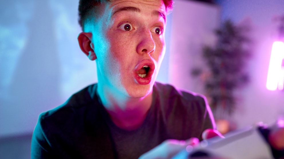 Junger Mann macht überraschten Gesichtsausdruck beim PlayStation-spielen.