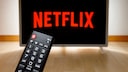 Netflix-Logo auf einem Fernseher, im Vordergrund eine Fernbedienung.