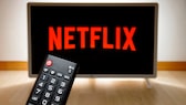 Netflix-Logo auf einem Fernseher, im Vordergrund eine Fernbedienung.