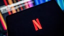 Netflix-Logo auf einem Tablet, im Hintergrund ein Fernseher.
