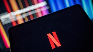Netflix-Logo auf einem Tablet, im Hintergrund ein Fernseher.