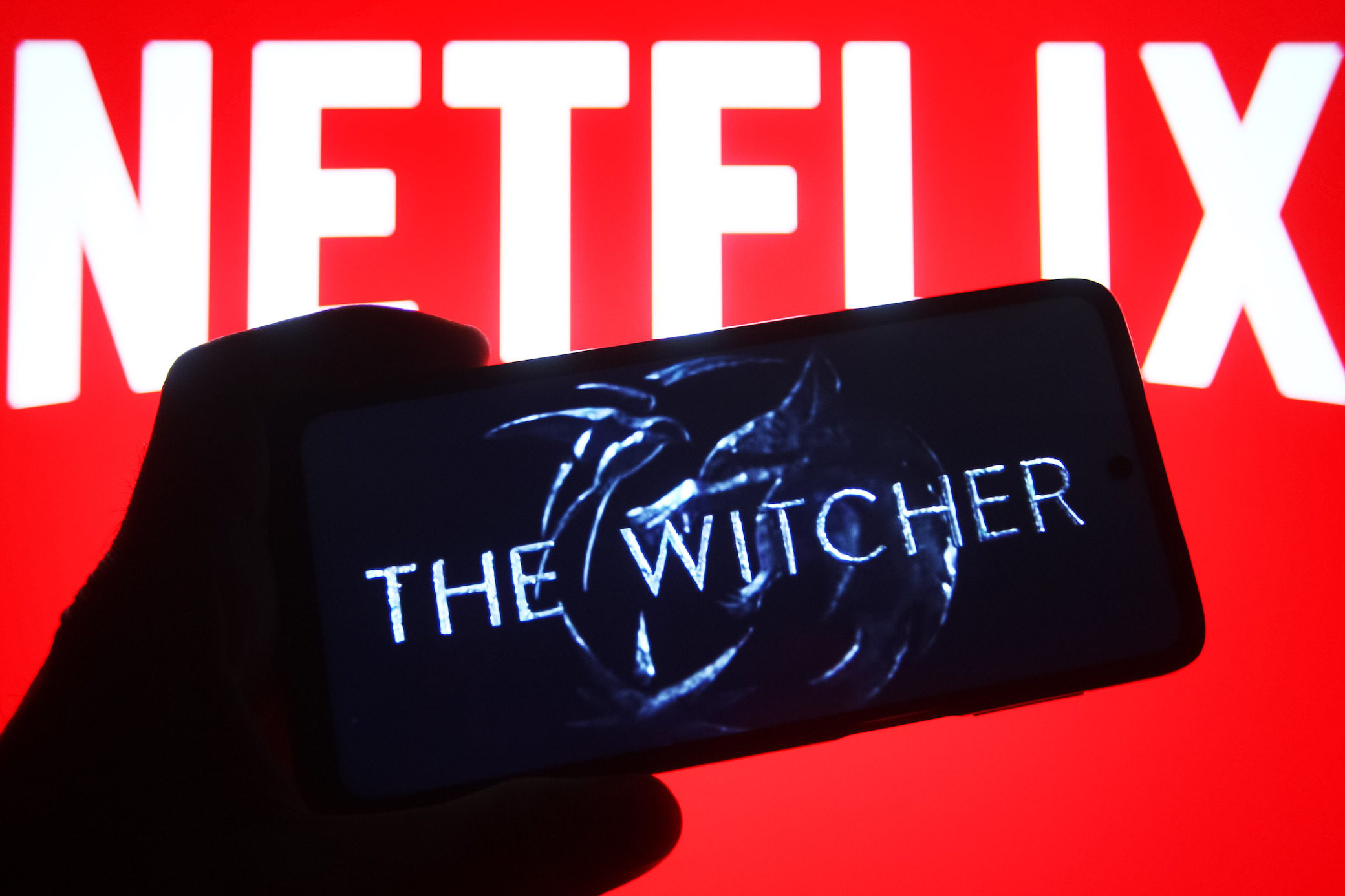 "The Witcher"-Logo auf einem Handy, im Hintergrund ein Schriftzug von Netflix.