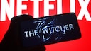"The Witcher"-Logo auf einem Handy, im Hintergrund ein Schriftzug von Netflix.