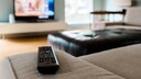 Aldi Samsung-TV Symbolbild: Fernbedienung liegt auf Sofa, im Hintergrund läuft ein Fernseher