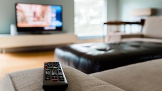 Aldi Samsung-TV Symbolbild: Fernbedienung liegt auf Sofa, im Hintergrund läuft ein Fernseher