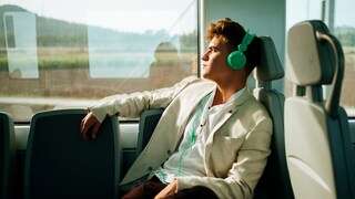 Symbolbild: Mann im Zug hört über Kopfhörer Musik.