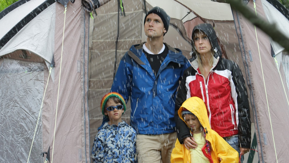 Familie steht bei Regen in einem Zelt und ist unglücklich.