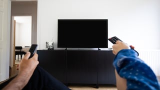 Menschen mit Fernbedienungen sitzen vor einem großen Fernseher mit wahrscheinlich 75 Zoll