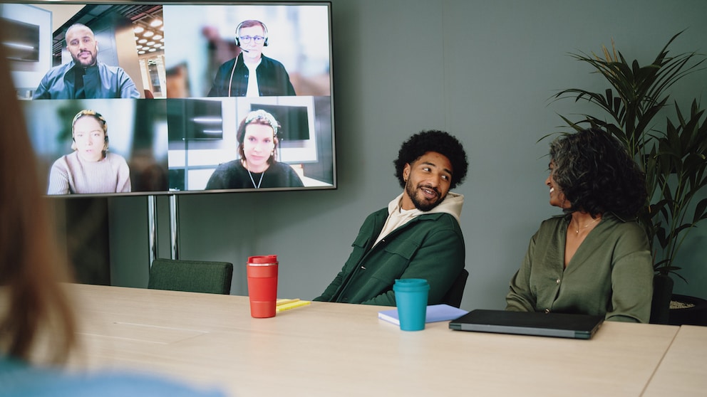 Symbolbild: Meeting in einem Konferenzraum mit Teilnehmenden offline und online