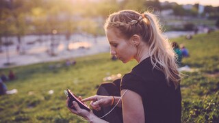 Symbolbild: Eine Sportlerin sitzt im Park und tippt auf ihrem Smartphone