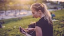 Symbolbild: Eine Sportlerin sitzt im Park und tippt auf ihrem Smartphone
