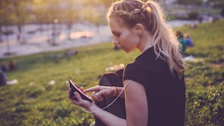 Symbolbild: Eine Sportlerin sitzt im Park und tippt auf ihrem Smartphone