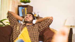 Symbolbild: junger Mann hört mit Kopfhörer auf dem Sofa ein Hörbuch