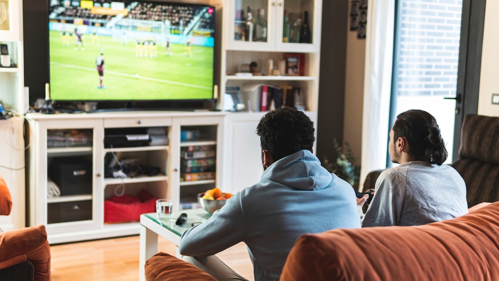 Symbolbild: Zwei Fußball-Fans schauen zuhause per TV ein Fußballspiel.