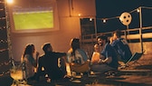 Symbolbild: Freundesgruppe schaut Fußball per Beamer auf einer Leinwand.