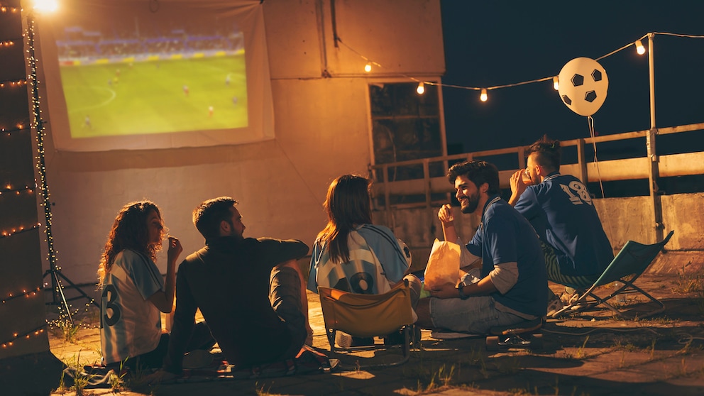 Symbolbild: Freundesgruppe schaut Fußball per Beamer auf einer Leinwand.