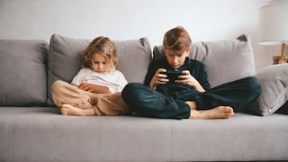 Zwei kleine Kinder auf dem Sofa mit Smartphone