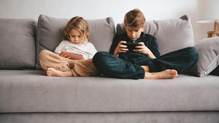 Zwei kleine Kinder auf dem Sofa mit Smartphone