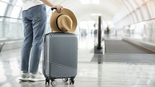 Jemand steht mit Koffer und Strohhut am Flughafen