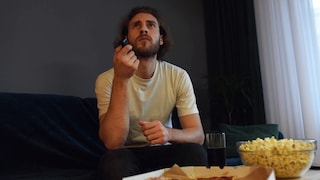 Mann sitzt mit skeptischem Blick vor dem Fernseher.