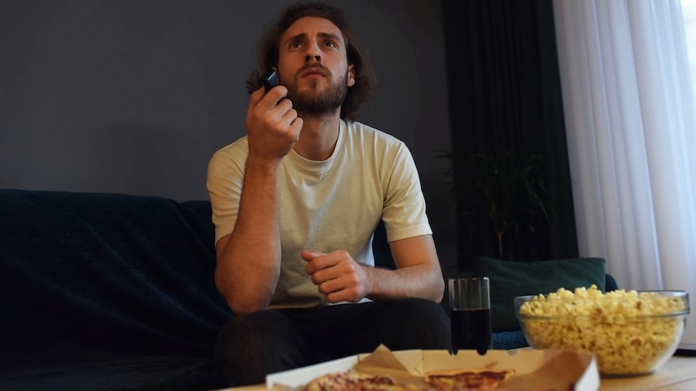 Mann sitzt mit skeptischem Blick vor dem Fernseher.