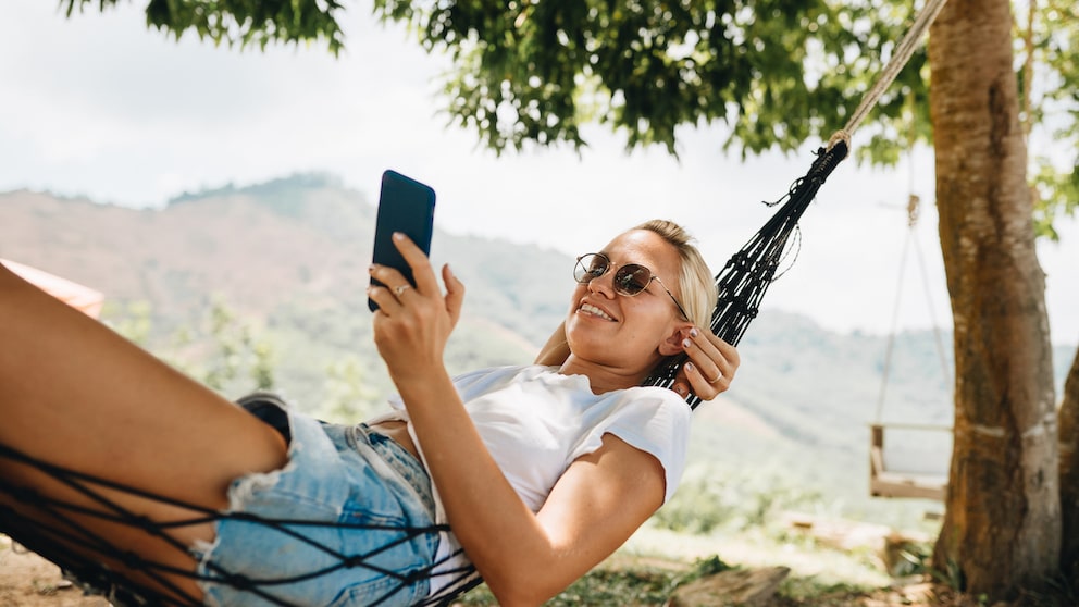 Symbolbild: Frau genießt mit Smartphone in der Hängematte ihren Urlaub.
