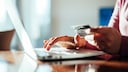 Person sitzt mit Kreditkarte in der Hand am Laptop