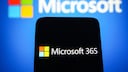 Microsoft 365 auf einem Handy, dahinter das Microsoft-Logo