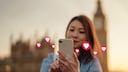 Frau schaut auf ein Handy, über dem Herzchen-Emojis fliegen