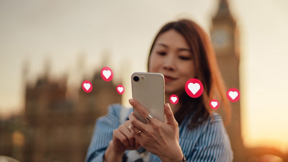 Frau schaut auf ein Handy, über dem Herzchen-Emojis fliegen