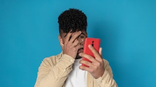 Mann schaut angsterfüllt durch die Hand auf sein Smartphone