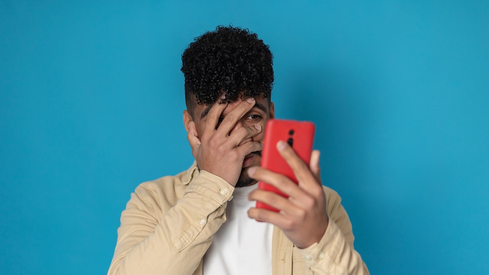 Mann schaut angsterfüllt durch die Hand auf sein Smartphone