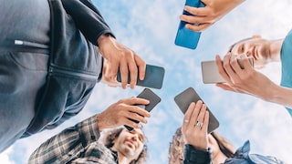 Gruppe Personen steht im Kreis und schaut auf ihre Smartphones