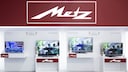 Das Metz-Logo an einem Messestand mit mehreren Fernsehern