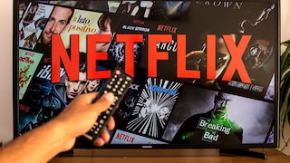 Person zeigt mit einer Fernbedienung auf einen Fernseher, auf dem Netflix zu sehen ist