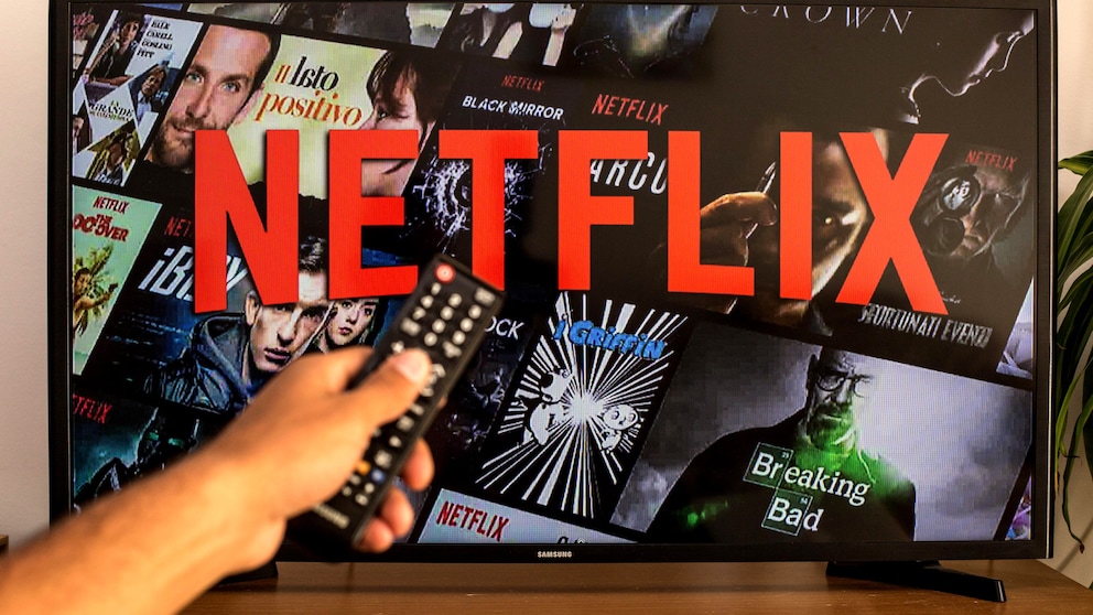 Person zeigt mit einer Fernbedienung auf einen Fernseher, auf dem Netflix zu sehen ist