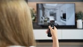 Frau mit Fernbedienung in der Hand vor einem 4K-Fernseher