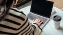 Frau sitzt mit einem Kaffee am Laptop