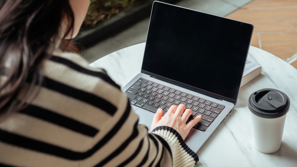 Frau sitzt mit einem Kaffee am Laptop