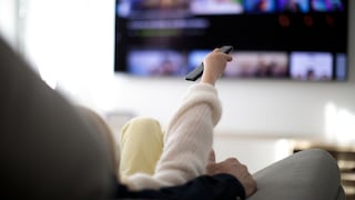 Frau mit Streaming-Fernbedienung vor dem Fernseher