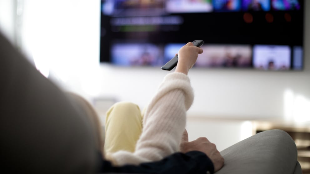 Frau mit Streaming-Fernbedienung vor dem Fernseher