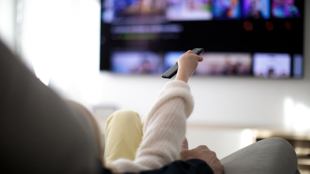 Frau mit Streaming-Fernbedienung vor dem Fernseher