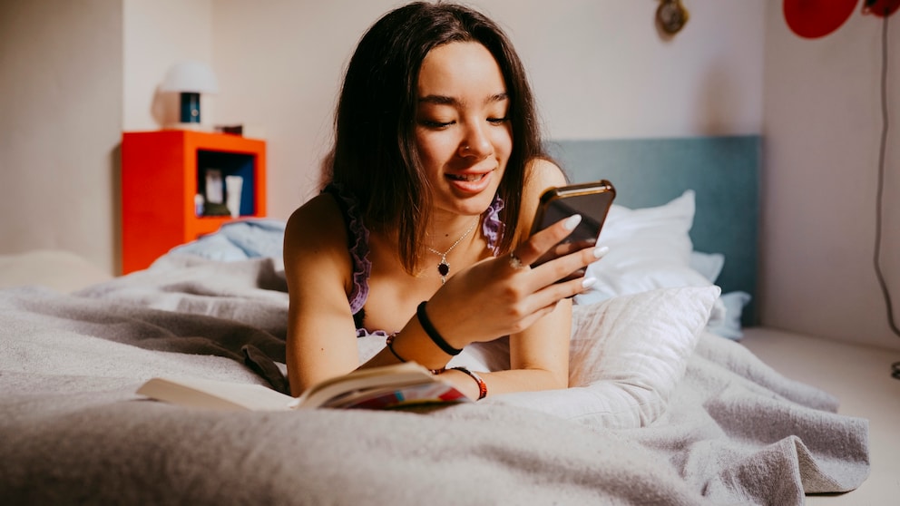 Frau liegt mit ihrem Smartphone in der Hand auf dem Bett