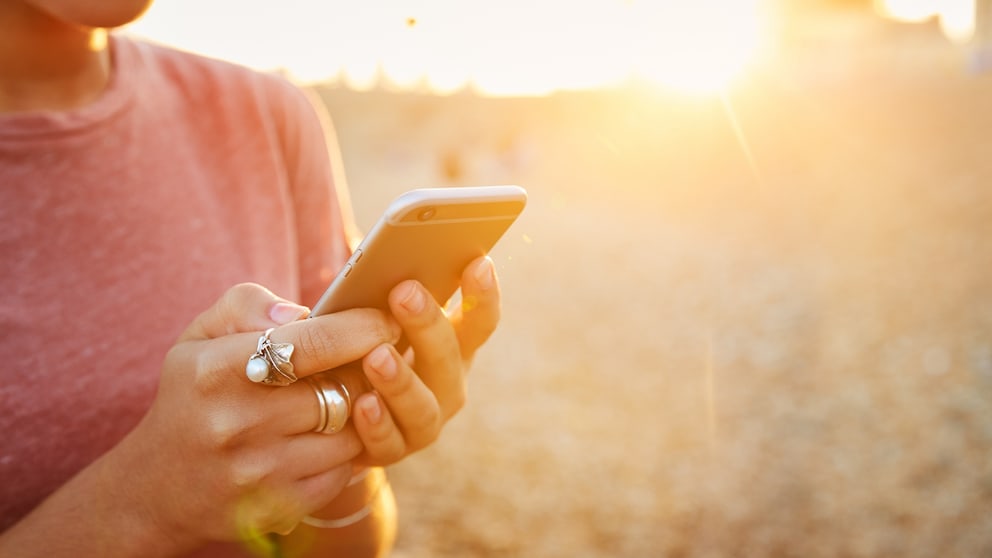 Frau steht am Strand und schaut auf ihr Smartphone