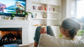 Frau sitzt mit Popcorn auf dem Sofa und sieht fern