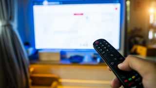 Person zeigt mit Fernbedienung auf einen Fernseher