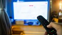 Person zeigt mit Fernbedienung auf einen Fernseher